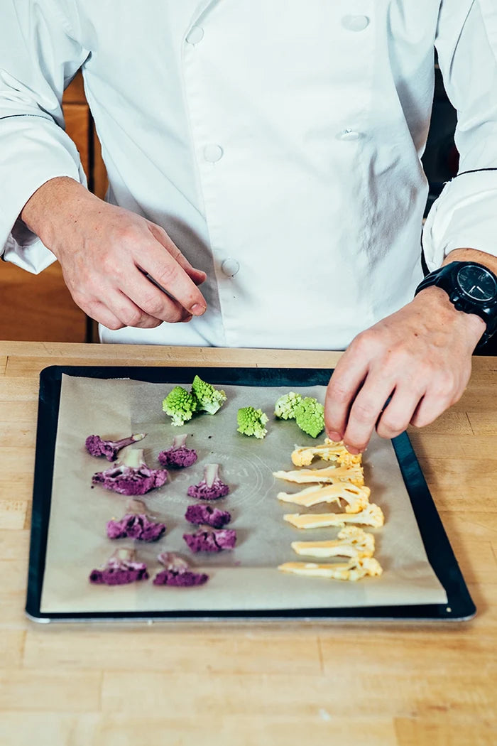 Chef preparing vegetables on a baking tray with a wooden surface