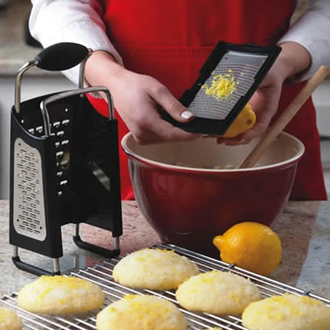 Person using a zester to grate lemon zest over cookies on a cooling rack.
