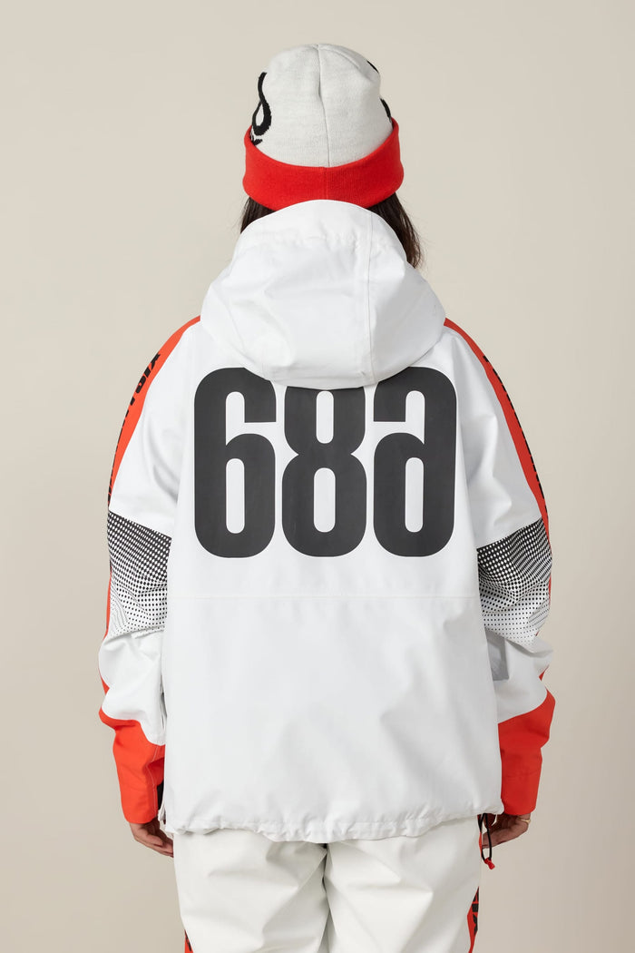 A person wearing the 686 Women's Fox Racing Shell Anorak by 686, featuring white and red colors and bold black "68a" lettering on the back, with white pants and a matching beanie, facing away against a beige background.
