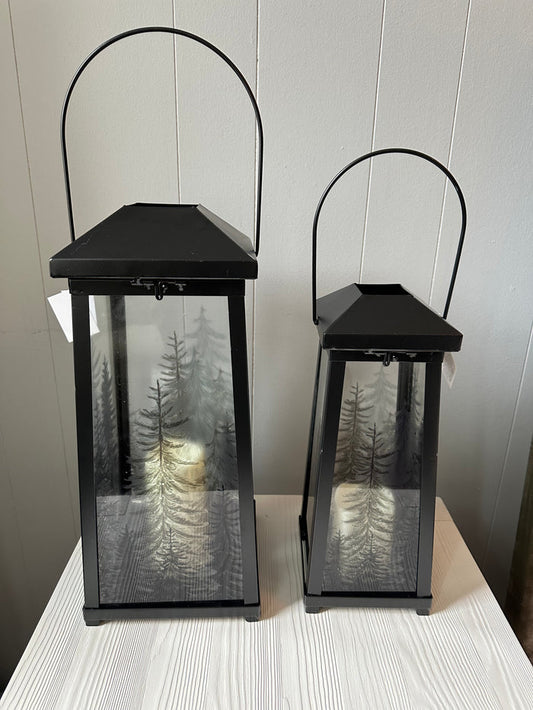 Two black LED candle lanterns with glass panels that have trees.