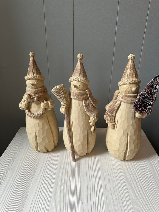Three decorative resin snowman figures with various accessories, placed on a white surface against a grey background.