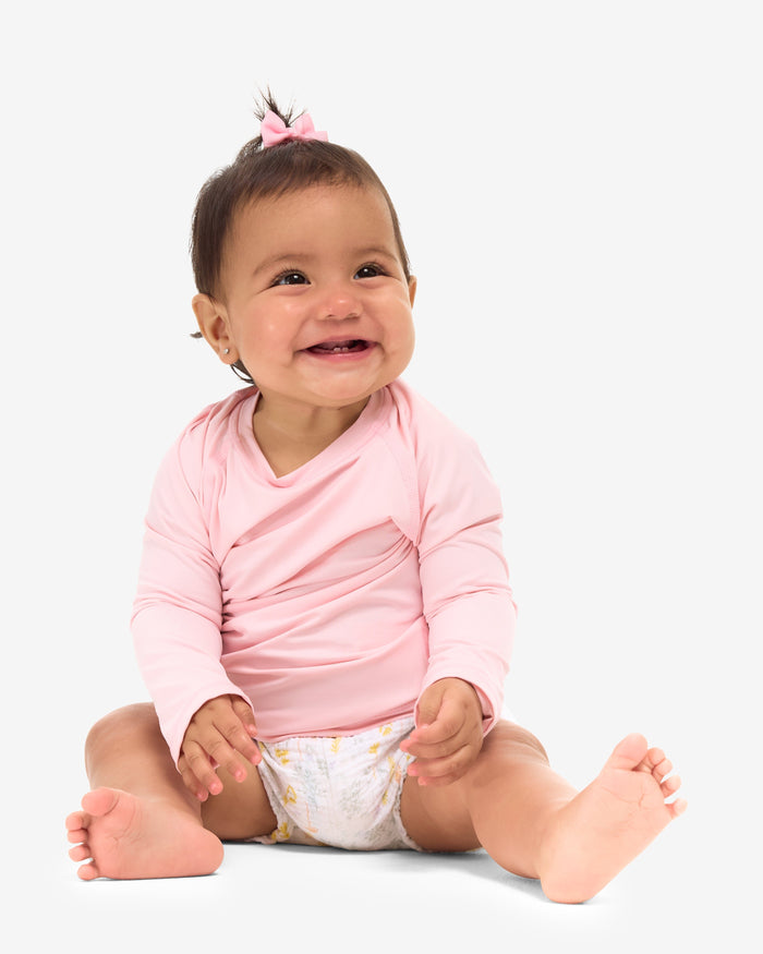 A baby in a pink long-sleeve sitting and smiling in front of a white background.