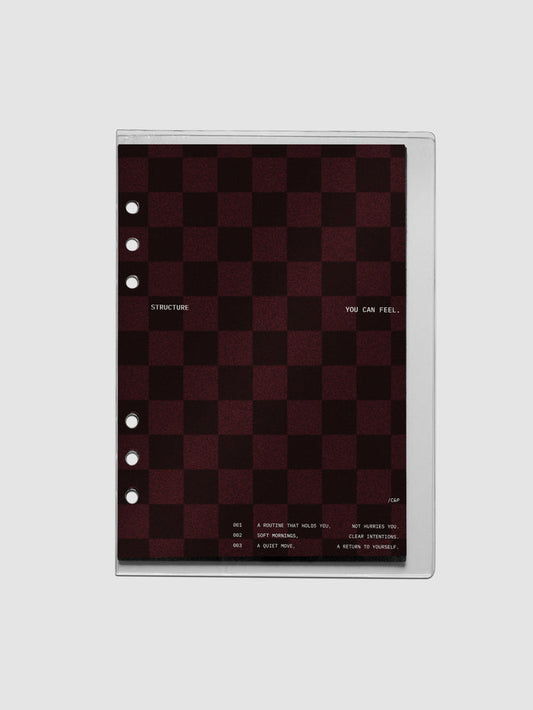 A5 sized velvet checkered dashboard in the color Bordeaux in between two crystal clear plastic planner covers with text printed on the cover on the theme of structure and routines.