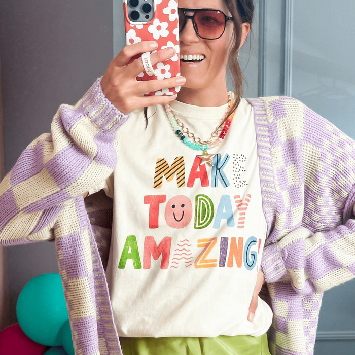 Person wearing a colorful 'Make Today Amazing' shirt in a room with balloons and a mirror.