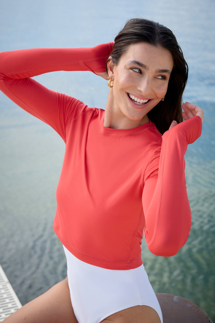 A woman wearing a red extended body length crop top on a white background