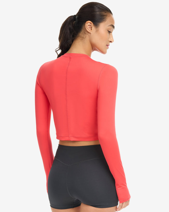 A woman wearing a red extended body length crop top on a white background