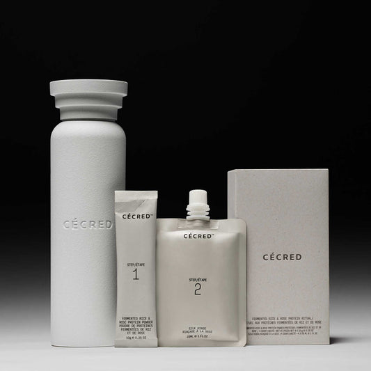 Cécred Fermented Rice & Rose Protein Ritual full set against a gradient grey background, including the Ritual Shaking Vessel, Step 1 Fermented Rice & Rose Protein Powder tube, Step 2 Silk Rinse pouch, and outer box packaging