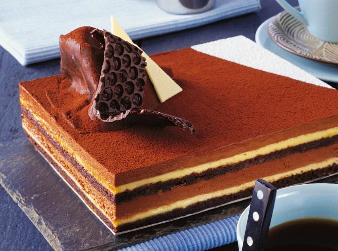 Layers of chocolate mousse cake with a coffee cup in the background