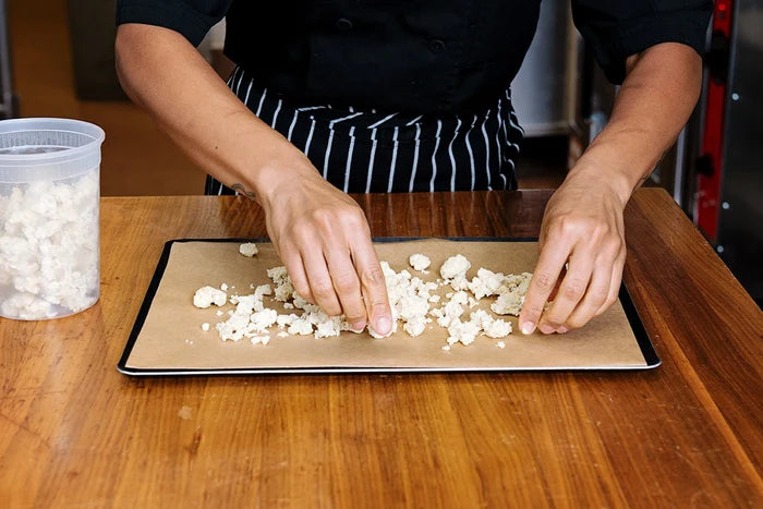 Chef laying down cheese on half sheet pan on wooden table.