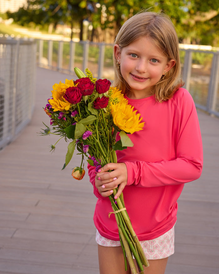 Young girl holding a bouquet of flowers on a wooden deck with trees in the background