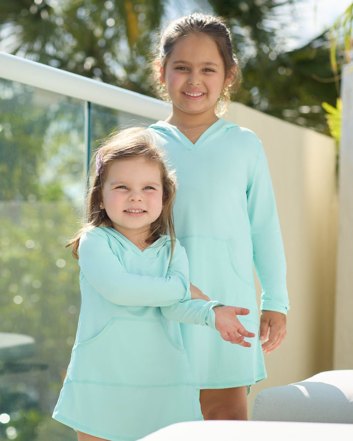 Two young girls in matching light blue outfits standing outdoors.