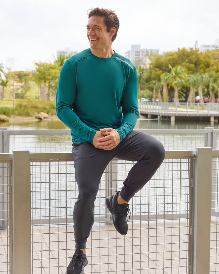 Man sitting on a fence by a lake with trees and buildings in the background
