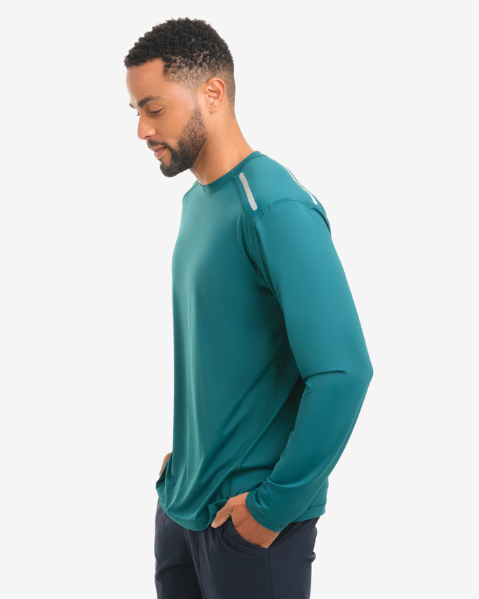 Man wearing a jungle green long-sleeve shirt and dark pants on a white background
