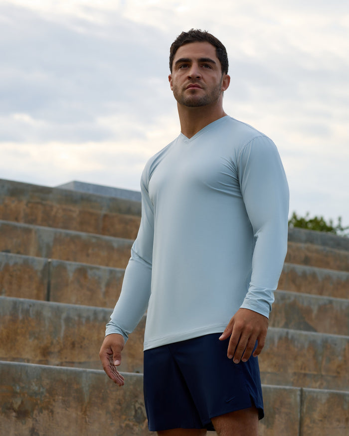 Man wearing a light blue long-sleeve shirt and dark shorts standing outdoors.