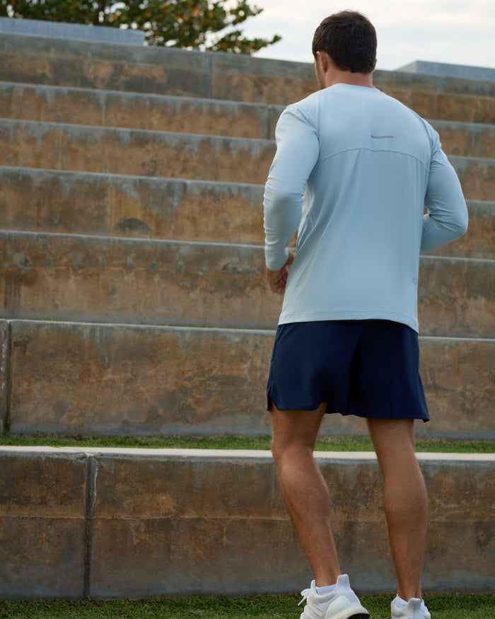 Person wearing a light blue long-sleeve shirt and dark shorts standing on stone steps.