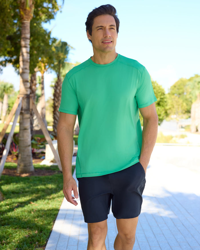 Man wearing a green shirt and black shorts walking outdoors on a sunny day.