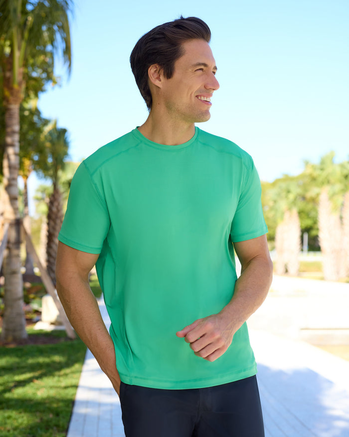 Man wearing a green shirt and black shorts standing outdoors with palm trees in the background