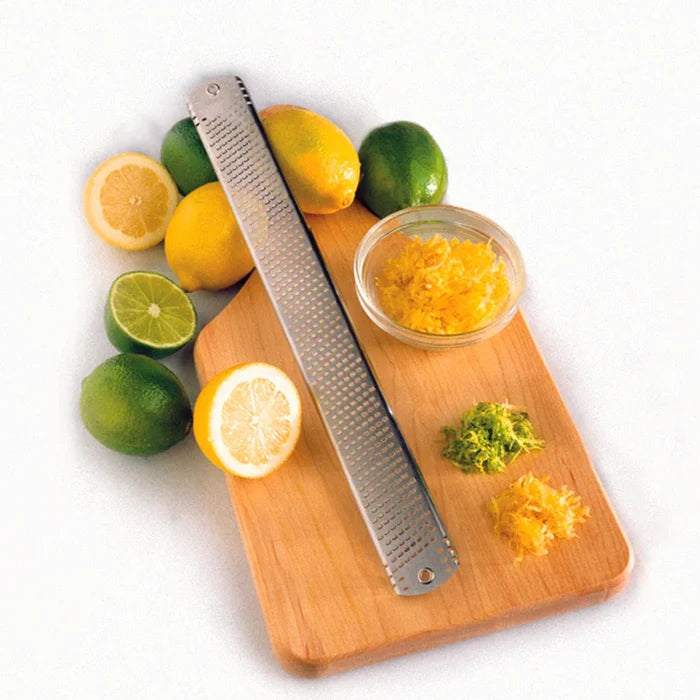 Zester on a cutting board with lemons, limes, and lemon zest in a bowl.