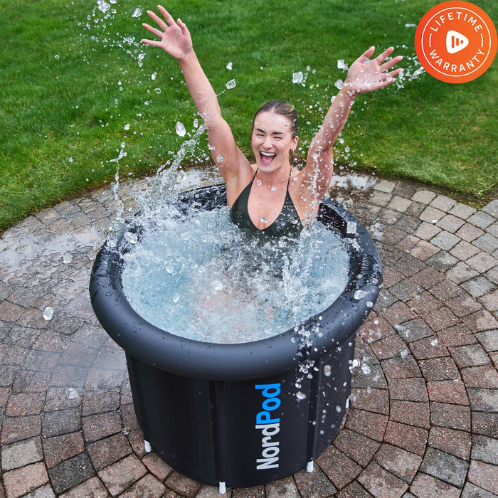 Woman celebrating with raised arms while sitting in the NordPod ice bath outdoors on a patio.
