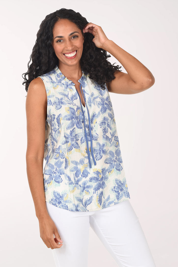 Woman wearing a sleeveless floral top and white pants on a white background
