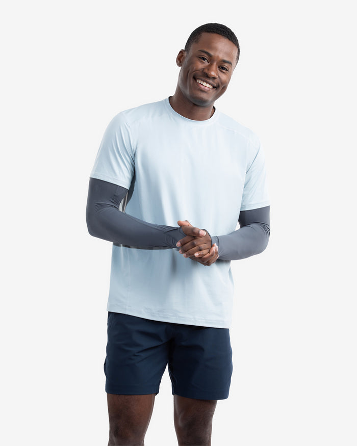 Man wearing a light blue athletic shirt with dark sleeves and navy shorts on a white background