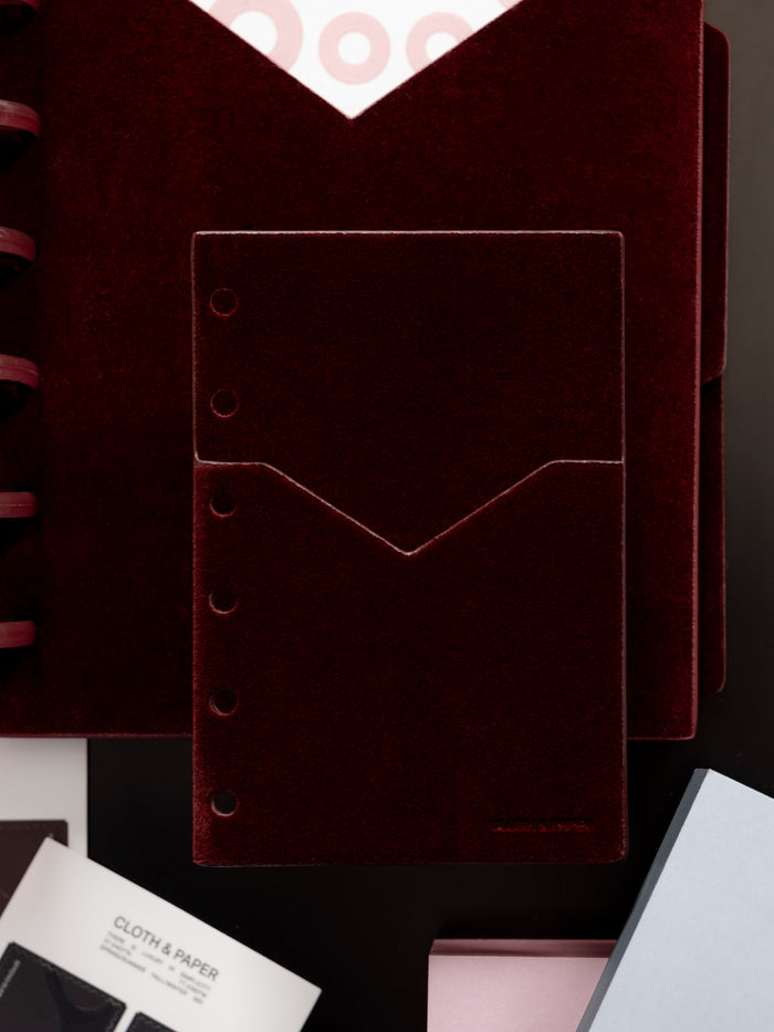 Velvet Pocket Folder in Bordeaux shown with other Cloth & Paper products against a dark background.