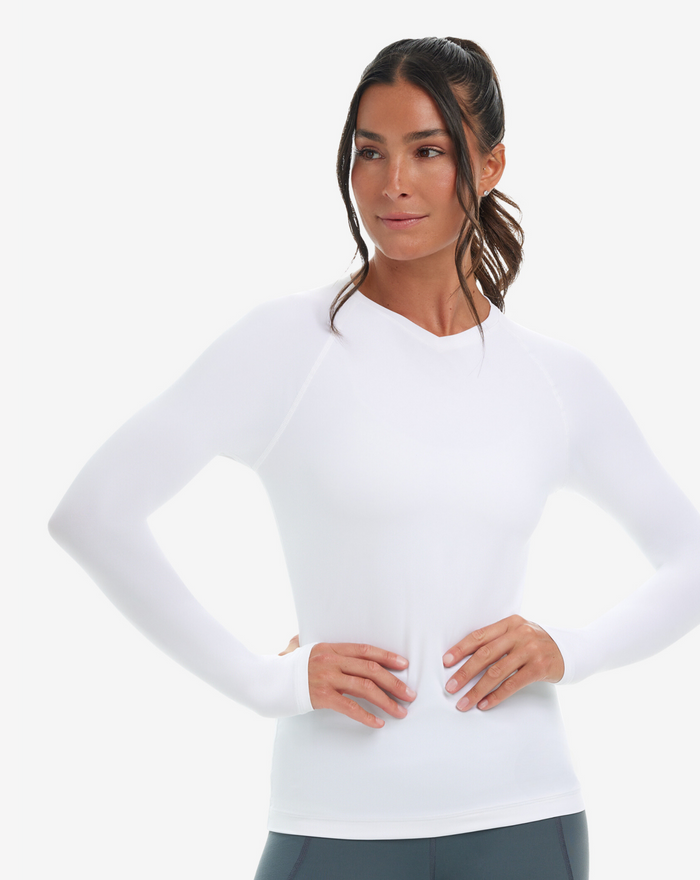 A woman wearing a white long-sleeved V-neck activewear top with thumbholes, on a white background.