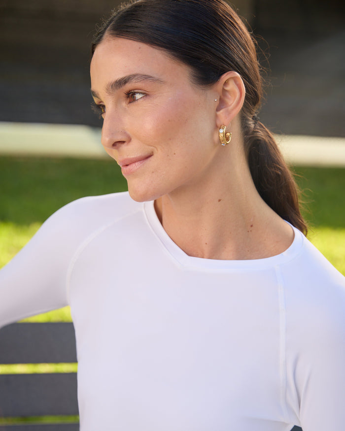 A woman wearing a white long-sleeved V-neck activewear top with thumbholes, at the park.