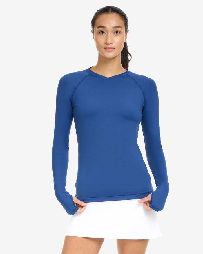 A woman wearing a blue long-sleeved V-neck activewear top with thumbholes, on a white background.