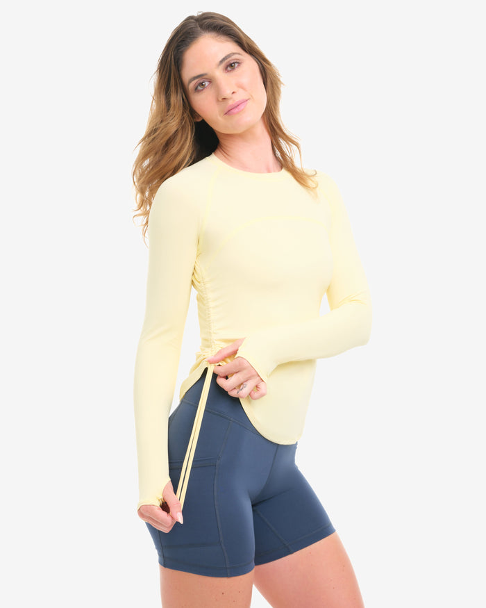 Woman wearing a yellow long-sleeve top and blue shorts on a white background