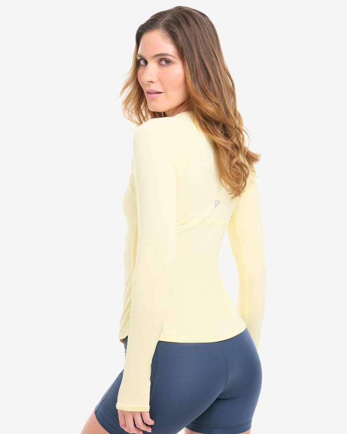 Woman wearing a light yellow long-sleeve top and blue shorts on a white background