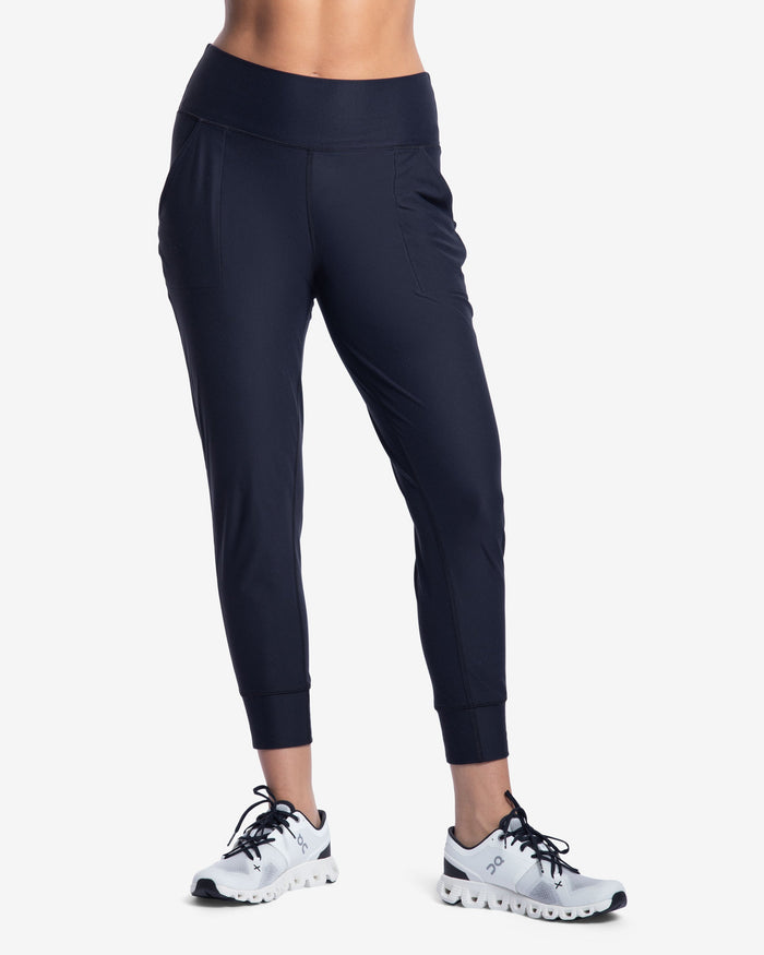 Person wearing navy jogger pants and white athletic shoes on a white background