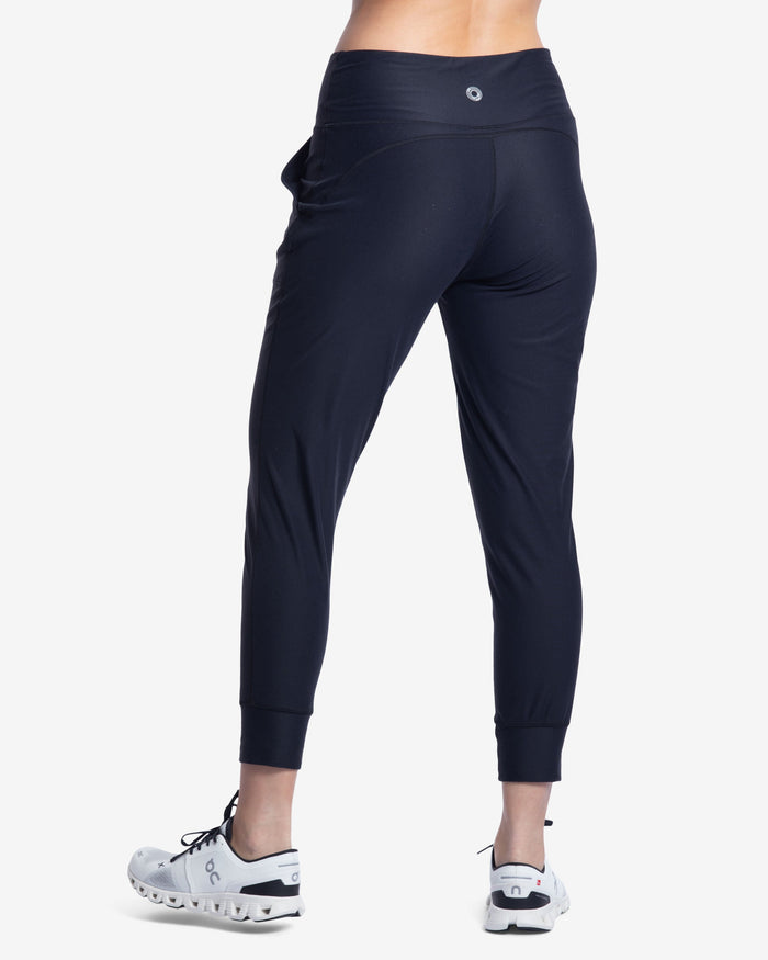 Person wearing navy jogger pants and white athletic shoes on a white background