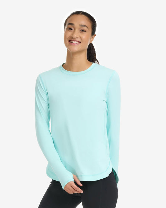 A woman wearing a green long-sleeved scalloped top with thumb holes, paired with black pants.